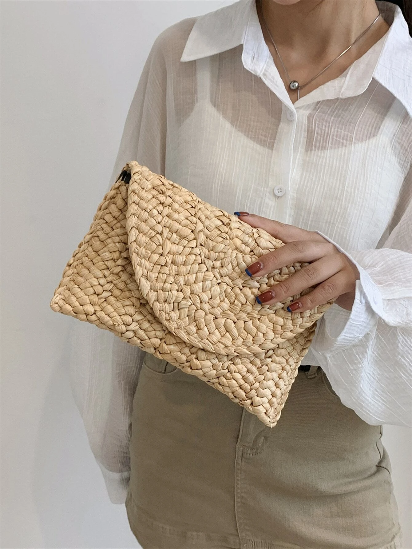 A woman elegantly holding our Amalfi clutch, showcasing its clutch design and organic straw material perfect for a sophisticated and timeless look