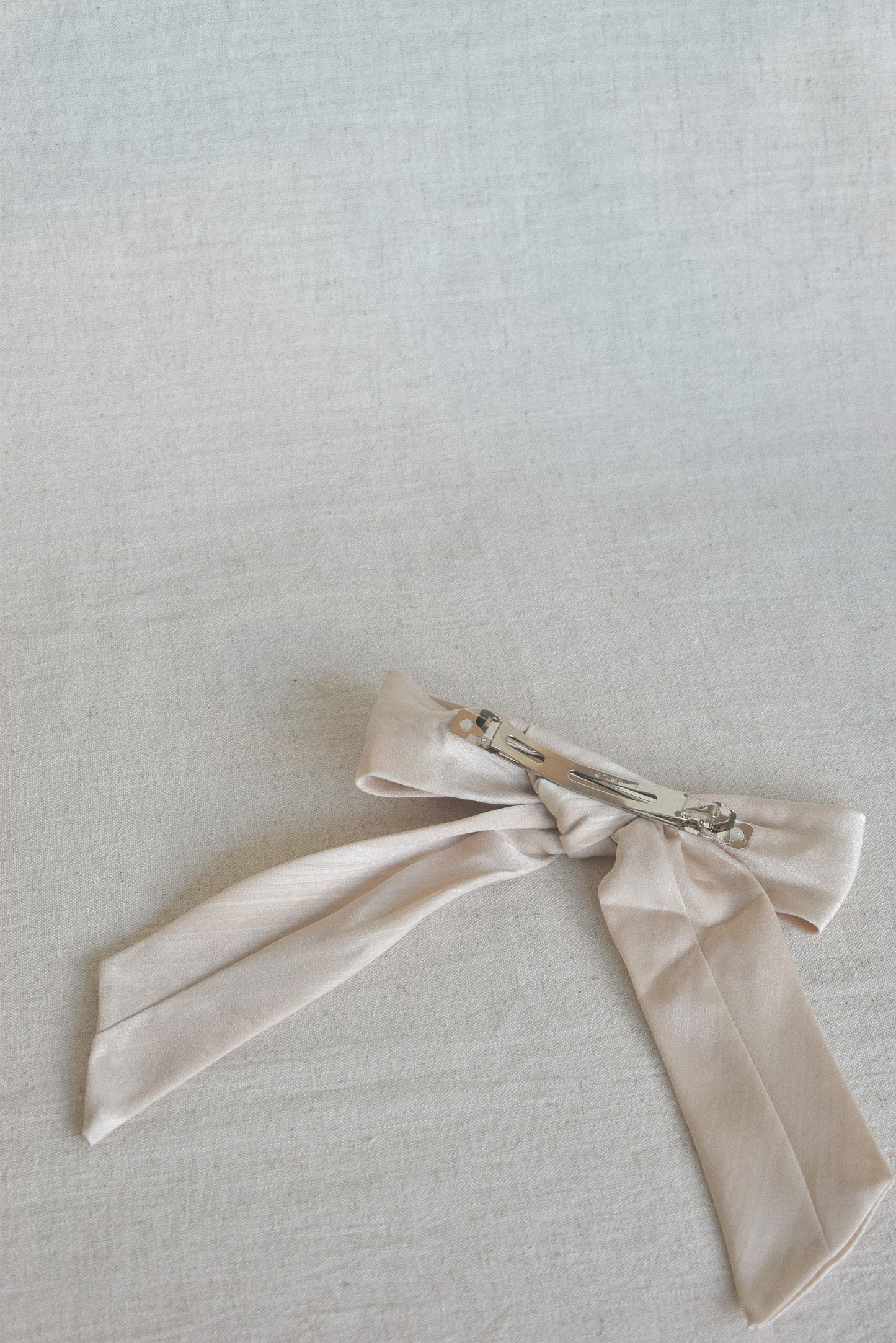 Back view of our Blossom Bow Hair Clip, laying flat on a neutral surface, showcasing its sturdy clip mechanism. Making it quick and easy to style with your outfit for wedding events