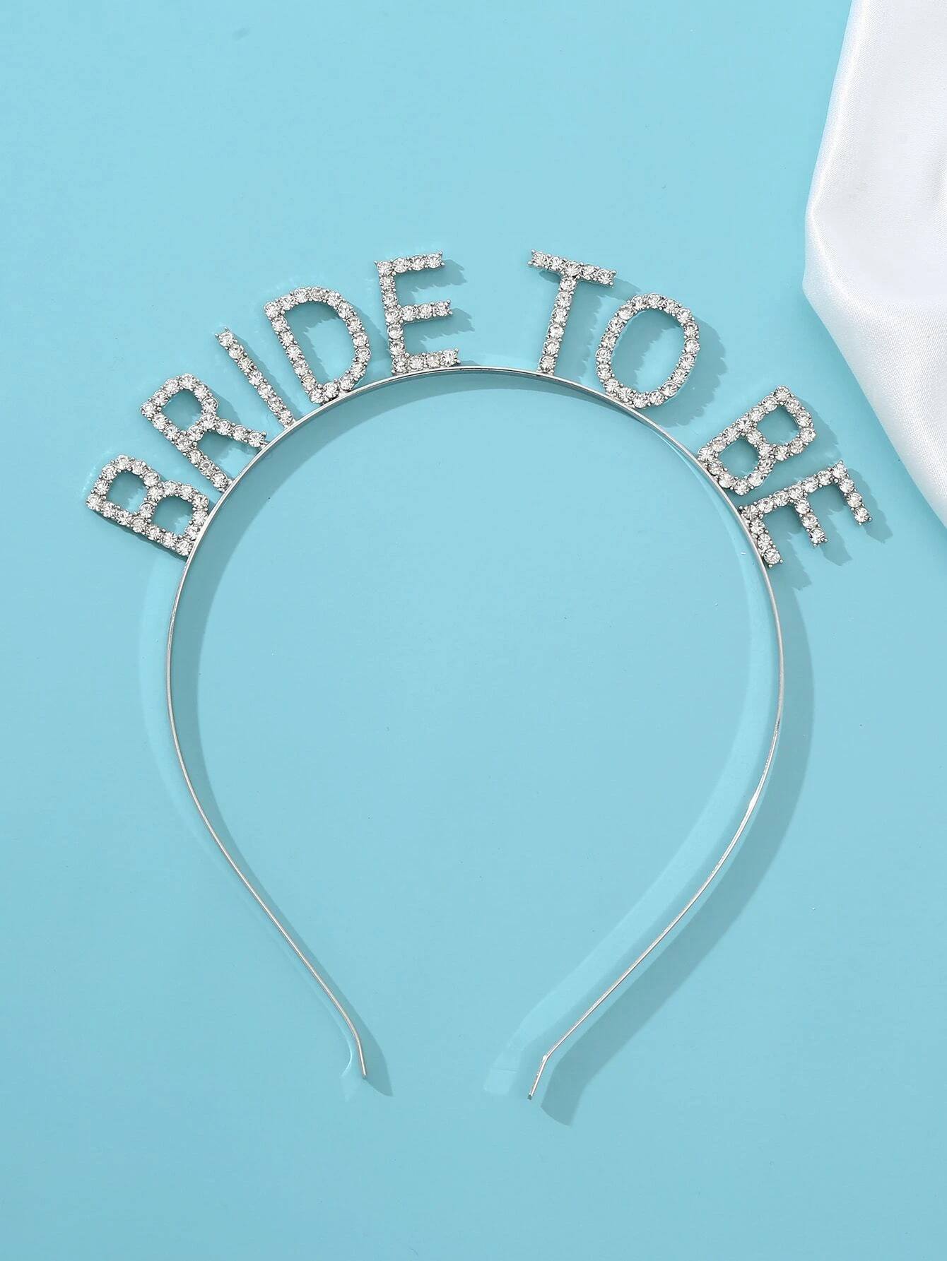 Bride-to-be Diamante Headband laying flat on a baby blue surface, which really compliments the silver headband and sparkle from the diamantes in the 'Bride-to-be' lettering. Adding elegance and sparkle to any bride for pre wedding celebrations or hen party.