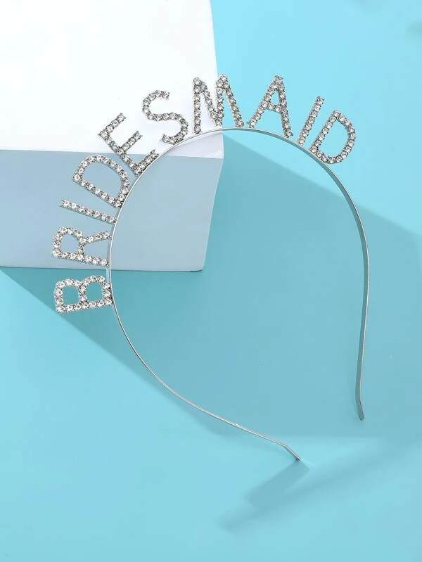 Our 'Bridesmaid' Diamante Headband resting on a white box on a baby blue surface. The silver headband lettering is detailed with diamantes, the angle of this shot highlights the sparkle. Perfect for bridesmaids to wear on the wedding day or during pre-wedding celebrations.