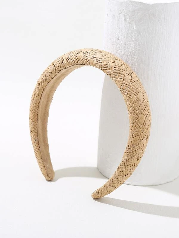 Angled shot of our woven capri headband, shown in neutral straw brown colour balanced against a white wooden plinth. Highlighting the padded band that adds a soft addition to and outfit for day to day events