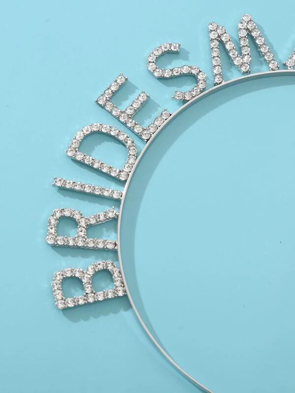 Close-up of the 'Bride' lettering in our 'Bridesmaid' Diamante Headband on a baby blue surface. Showing the sparkle from the diamante rhinestones lettering. Adding glamour to every bridesmaid for pre wedding celebrations.