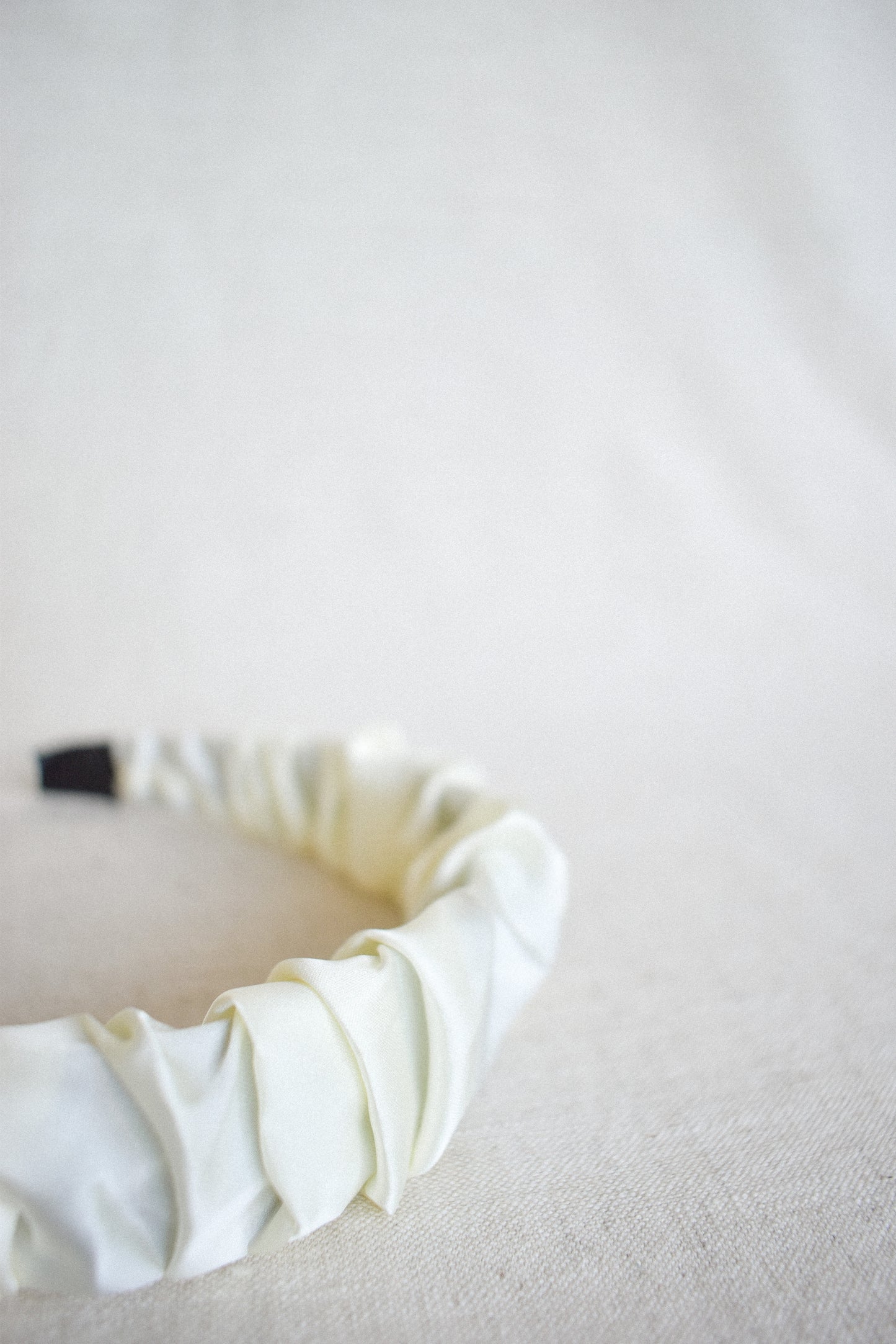 Close-up of our Calla Headband on a neutral linen surface, showcasing its elegant ruffled satin/silk fabric design. Versatile with any outfit for your next event day/evening and brides