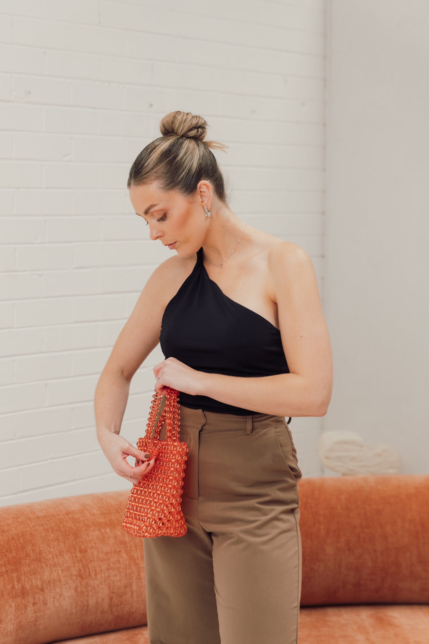 Coral holding our salmon/pink beaded bucket bag, highlighting the clasp to close the bag. She has paired this with smart brown trousers and chic black top, perfect for when you have work followed by after work drinks
