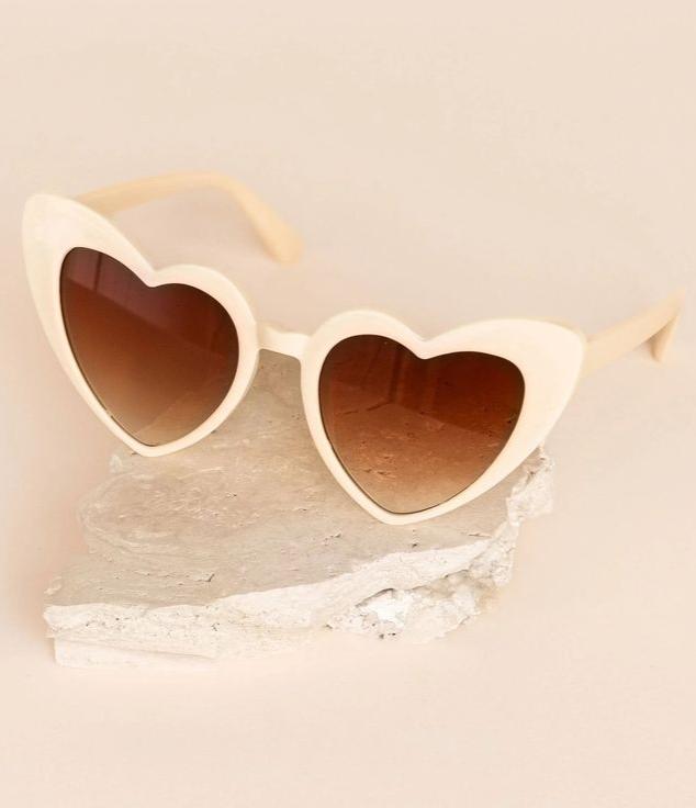 Our cream heart shaped sunglasses, against a stone neutral background. Lenses showing a gradual hue, creating a softer look. Perfect for bridal parties and activities