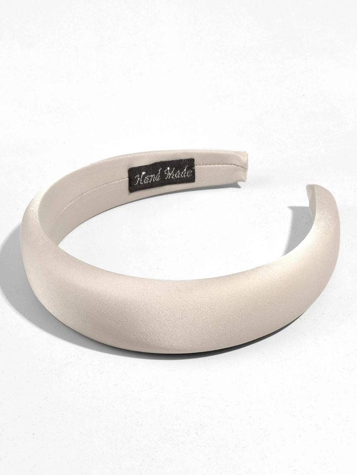 A shot showing our Creme headband HANDMADE label, cream satin/silk elegance. Band is laying down flat on a white surface. Highlighting the material quality and perfect for all classy evening events or spring races