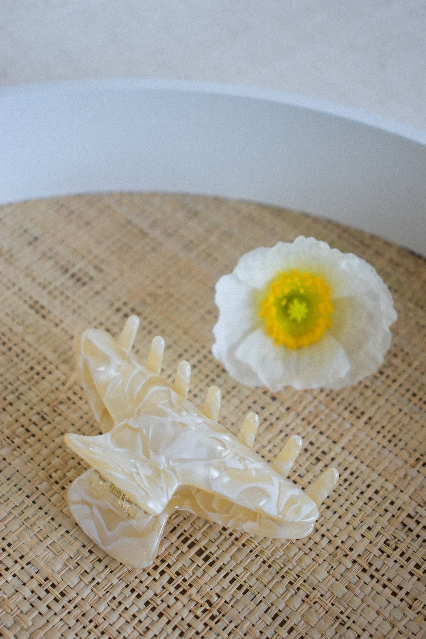 Our Flora hair clip laying flay on a straw surface next to a white and yellow flower, highlighting the clips pale buttery yellow colour. Soft and practical for your next event