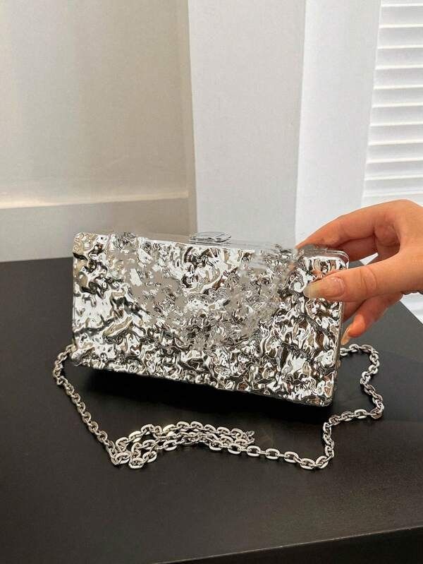 Our Lexi Chrome mirror-textured acrylic clutch bag, being held at an angle to highlight the shine of the design. Shown here with the silver chain shoulder attachment. A fun addition to any outfit for your next event