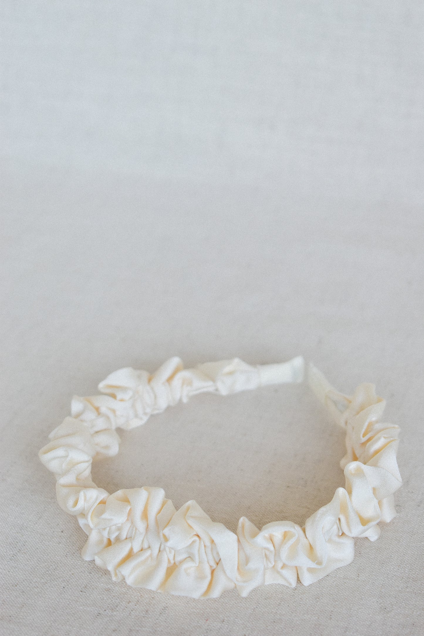Our Lily headband laying flat, showing a close up of the soft cream ruffled design of the satin/silk material. From ear to ear this design will be a cute addition to any outfit. Perfect for any bridal party or bride on the wedding day.