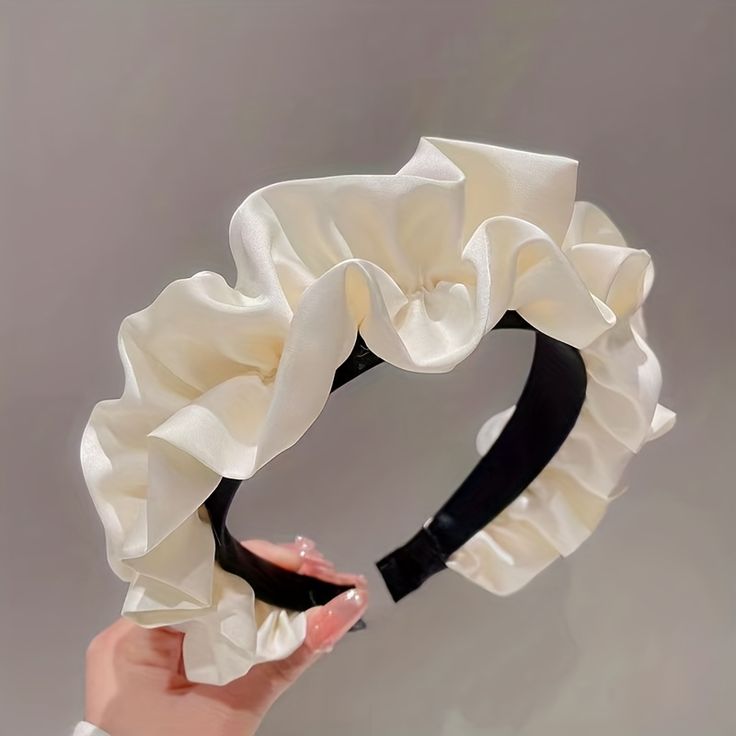 Our Lotus headband being held by a woman, showing a close up of the soft ruched design and cream silk/satin material across the whole band. Against a neutral grey background, highlighting the cream colour. Perfect for brides/bridesmaids