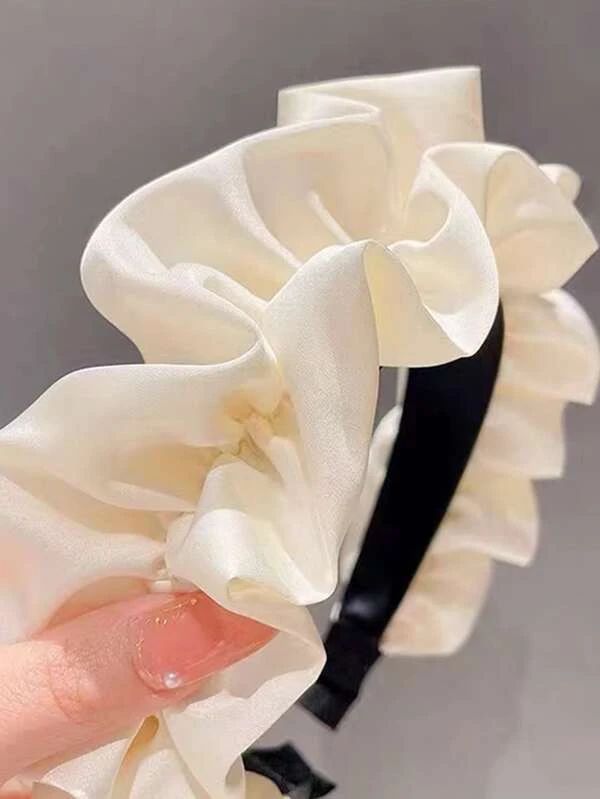 Our Lotus headband being held by a woman, showing a really close up shot of the soft ruched design and cream silk/satin material across the whole band. Perfect for brides/bridesmaids or adding a softness to any day event outfit