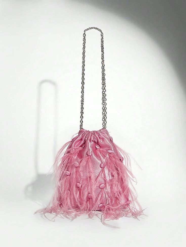 Our Lulu bag against a white background, showing its light pink velvet, drawstring design with soft staggered feathers on one side, with a medium sized silver chain handle. Perfect for adding a pop of colour to your next outfit