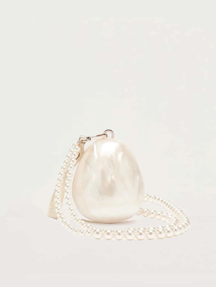 Our Peggy Bag pearl white acrylic egg-shaped mini bag, shown against a white background. Versatile interchangeable handles, as a clutch with a small cream leather wrist strap or a cross body pearl beaded shoulder bag. The ultimate bridal accessory or statement event bag.