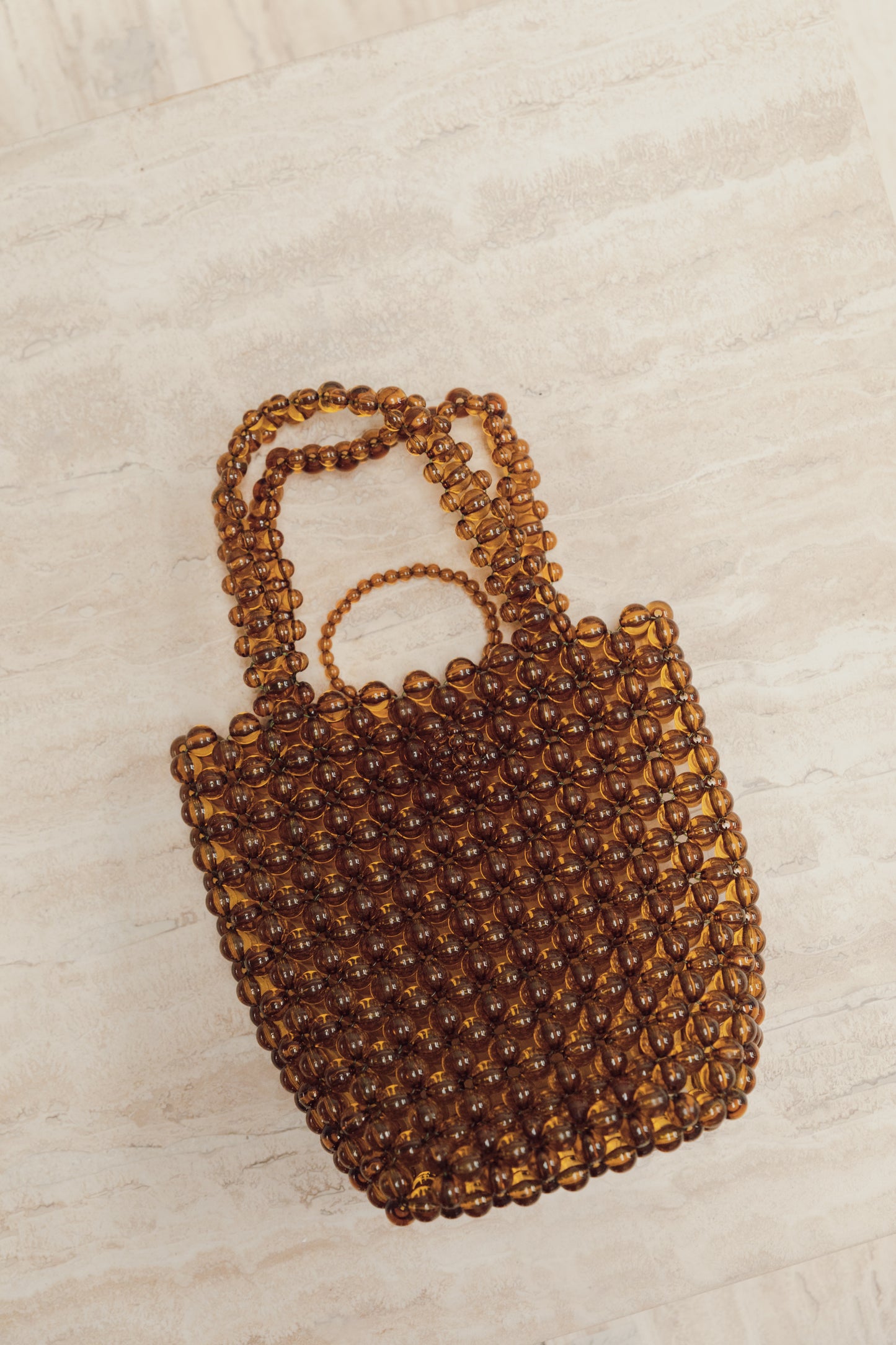 Our Olive khaki clear beaded bag with a loop over to close clasp and a short over the forearm beaded handle, shown laying flat against a neutral background. Highlighting the flexibility of the beaded bag. Effortlessly elevates your party outfit day or night