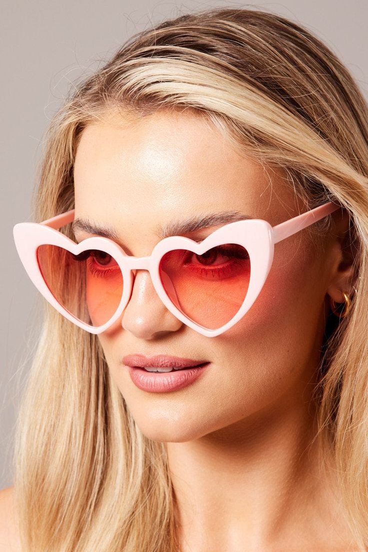 A blonde woman wearing our Pink on Pink Heart Sunglasses against a neutral background. These come in various colours, highlighting here the pale pink colour with pink lenses, heart-shaped glasses. Perfect for bride or bridesmaids at your next hen party or fun festival event