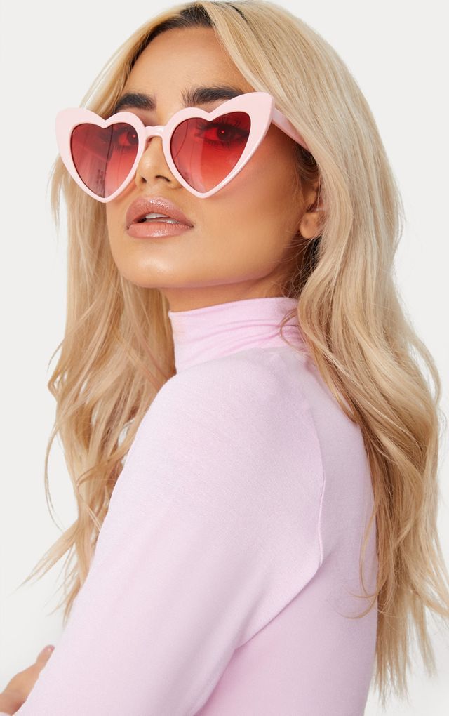 A blonde woman wearing our Pink on Pink Heart Sunglasses against a white background. These come in various colours, highlighting the pale pink colour with pink lenses heart-shaped glasses. Perfect for bride or bridesmaids at your next hen party