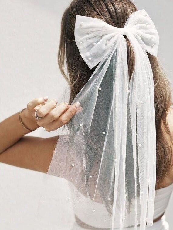 Our faux pearl detailed bow, shown styled in the hair, Highlighting the length of the bow which gives a veil vibe. Enhance your wedding hair for
a timeless look