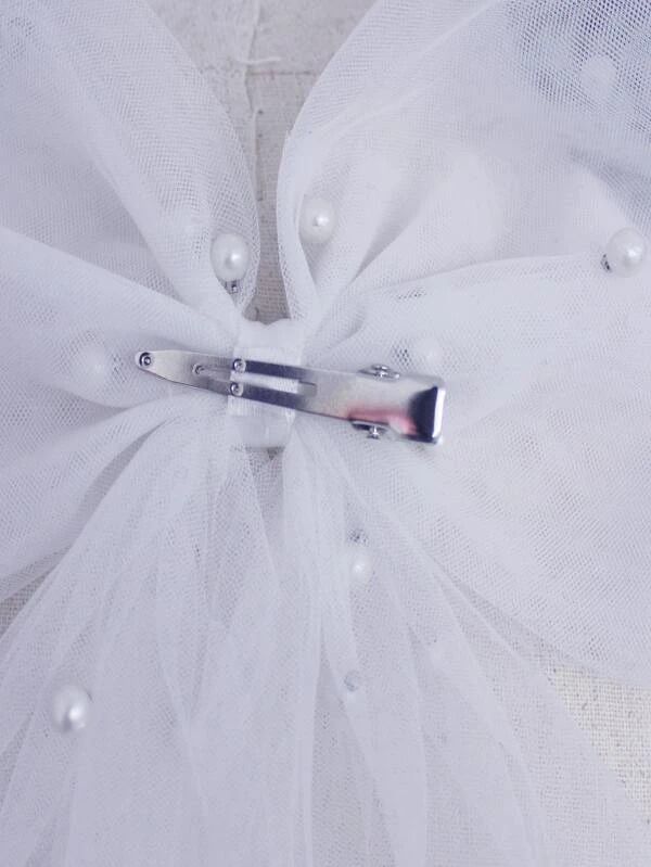A close up of the secure silver clip of our Rosie Pearl Bow, showing the mesh veil fabric and scattered pearls, that hides this clip fastening. A timeless addition for all bride to be's