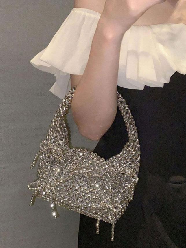 A woman holding our Scarlett bag over her forearm, showing the size and structure of the bag and the thick handle. This bag is made up completely of silver beading with added silver beaded bows scattered across the bag. Adding shine and sparkle to your next event outfit.