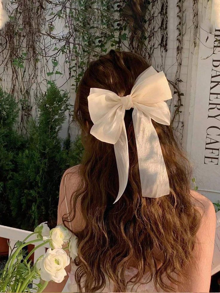 A woman wearing our Sweet Pea Bow Hair Clip under a sunset glow lighting, highlighting the softness of the sheer cream fabric and double layer bow, adding a delicate addition to all brides.