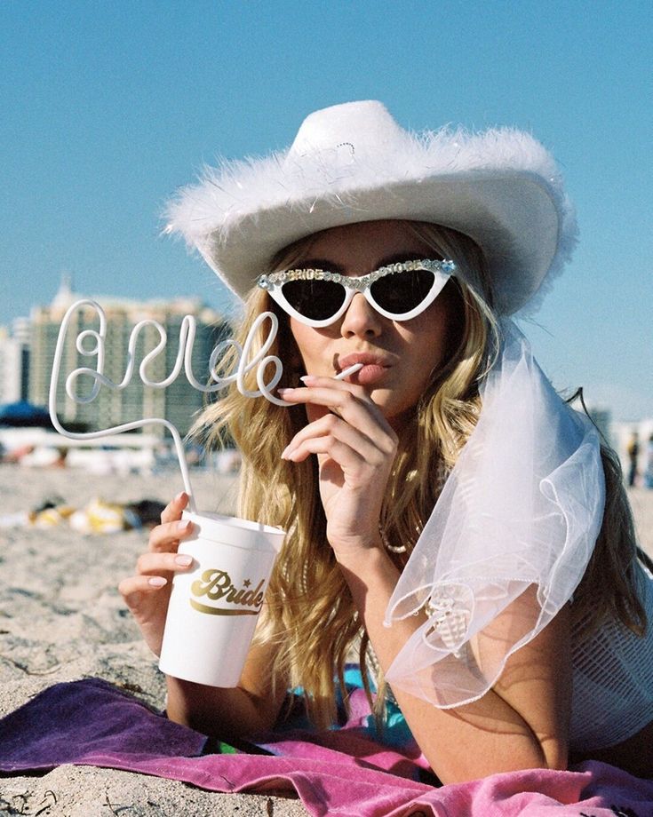 A bride using our White BRIDE straw on holiday, wearing a white fluffy cowboy hat. Highlighting the height of the straw and the large BRIDE lettering. The perfect fun addition for any hens party