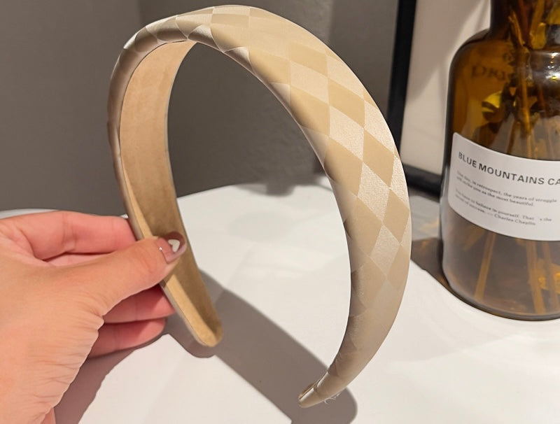 Close up of woman holding our Florence soft latte satin/silk headband. Showing the texture of the checked design. Perfect for day to day occasions