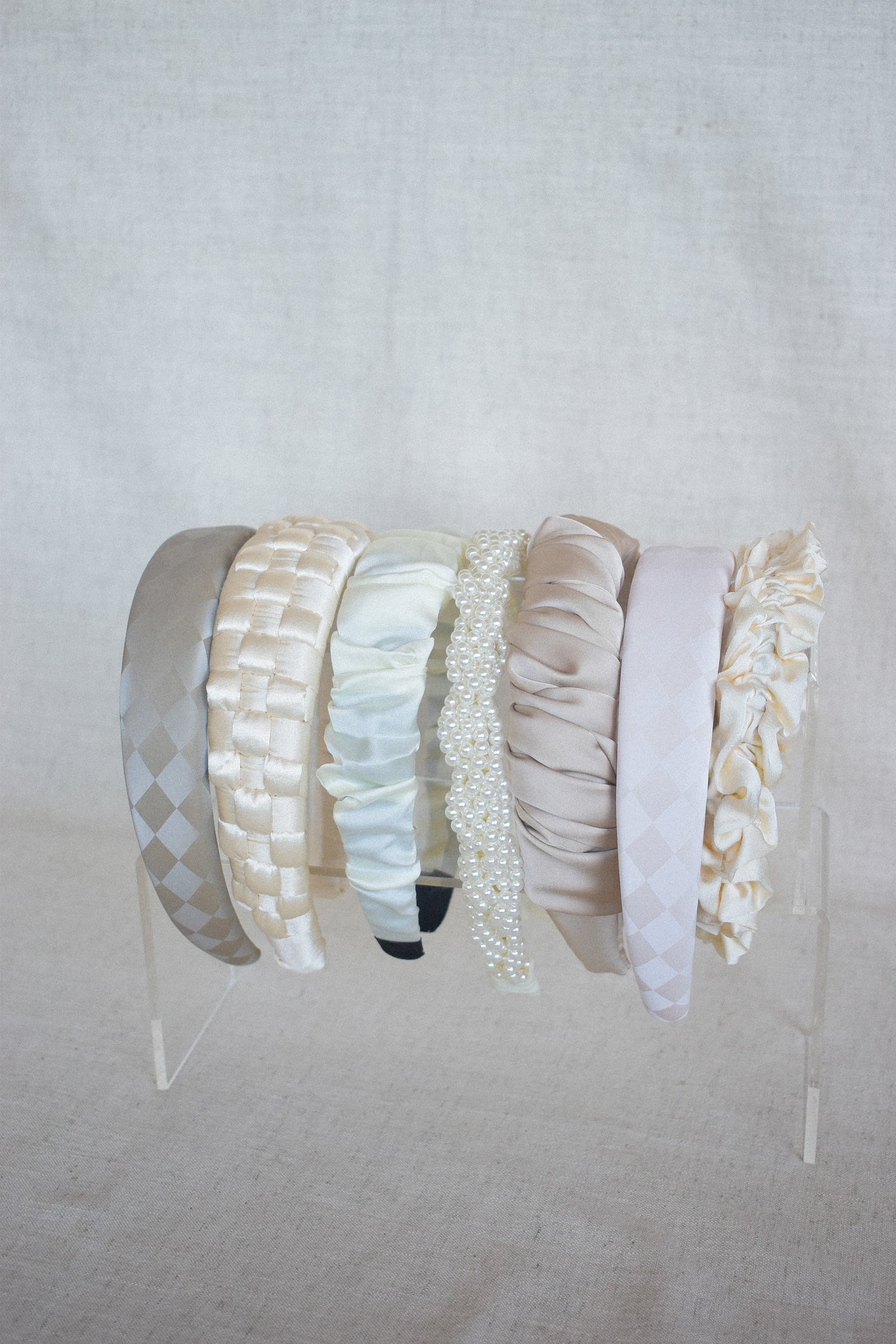 A line up of various neutral/champagne/latte/cream/ivory coloured headbands. Cloud, is located third from the right of the line up. Highlighting the sheen of the fabric and the latte colour. perfect for bridal and wedding events
