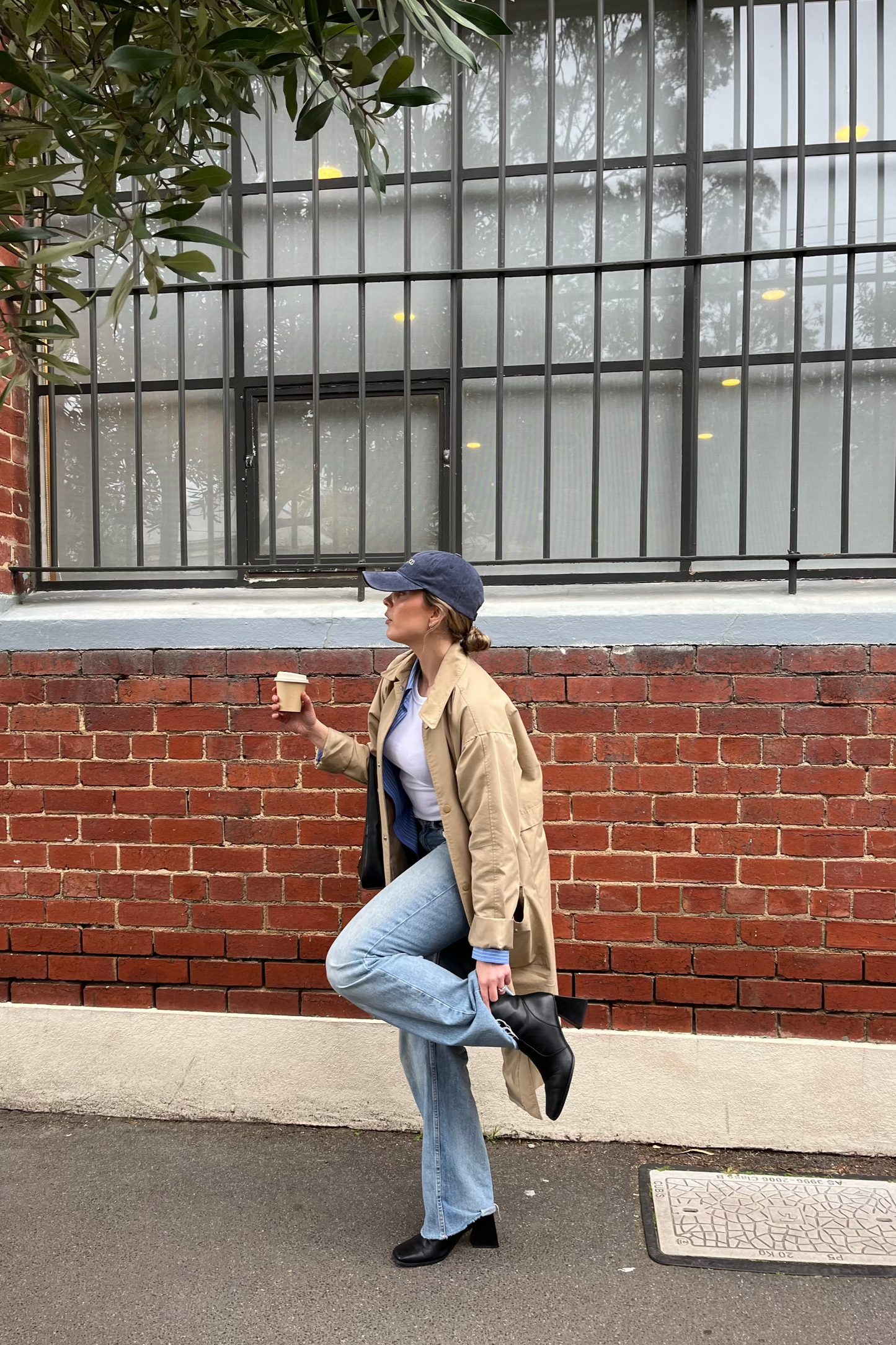 Coral wearing a Blueberry Pie Cap with a brick wall and glass window behind her. Showcasing the profile angle of the faded denim blueberry coloured cap. Perfect for a casual outfit