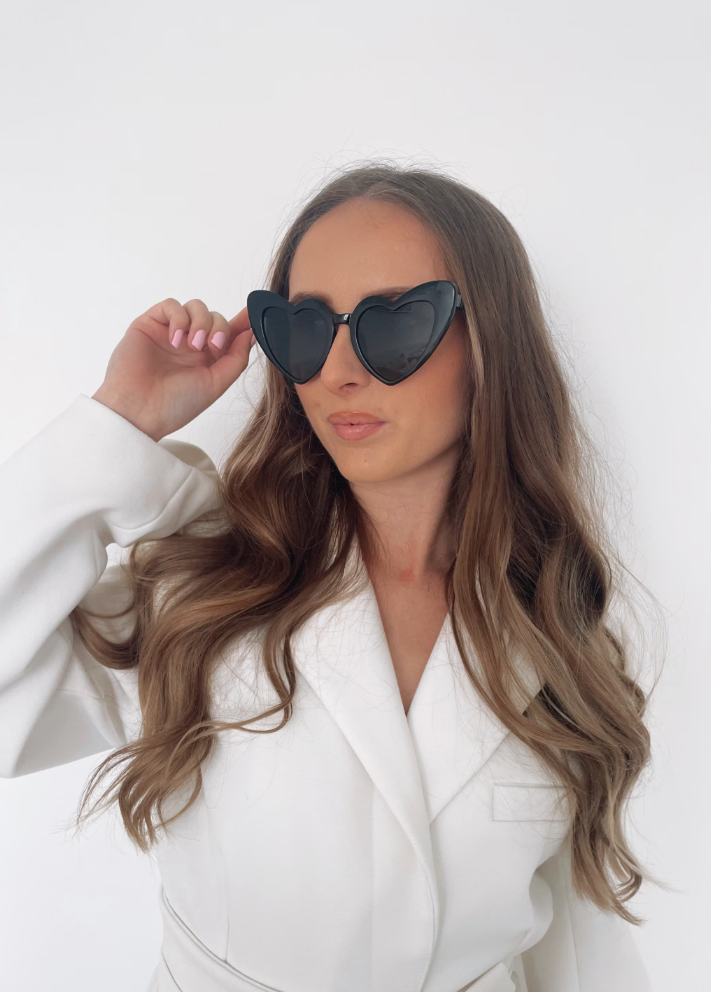 A woman wearing our Black Heart shaped sunglasses wearing a white shirt. These add a fun touch to her look day to day and are perfect for hen parties.