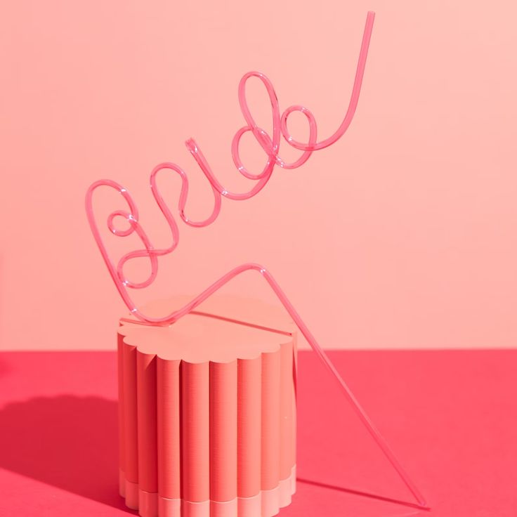 Our pink BRIDE straw against a shaded pink background, balanced on a plinth. Highlighting the height and colour of the straw and the large BRIDE lettering. The perfect fun addition for any hen/bachelorette party