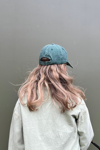 A shot of a woman wearing our Green Goddess Cap from behind. Dark green faded denim and featuring a bold fluro green embroidery. Perfect for casual daily wear for all hair colours and types