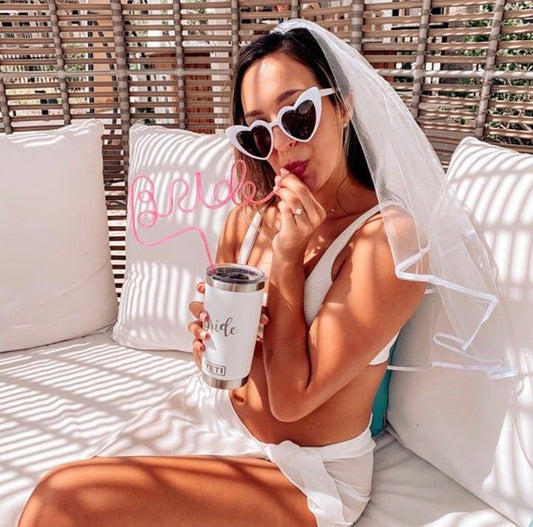 A bride using our pink BRIDE straw on holiday, wearing a white veil. Highlighting the height of the straw and the large BRIDE lettering. The perfect fun addition for any bridal party decor.