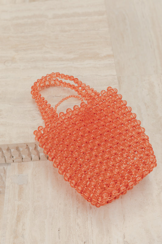 Coral pink bucket handbag made entirely of small beads, against a neutral background. Functional and fun addition to your next outfit you can dress up or dress down. 