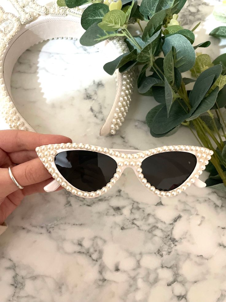 Our Cat eye pearl sunglasses being held against a marble background with matching pearl headband. Showing that you can easily pair and match these sunglasses with any other pearl accessory for any bridal event. Highlighting the size of the glasses for comparison