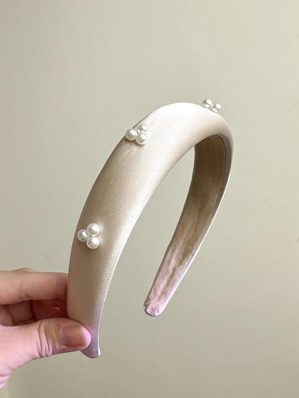 Our Champagne coloured satin padded headband with small clustered pearl detail across the band. Band is held up against an neutral background, highlighting the sheen of the satin that will add softness and touch of glamour to any outfit day or night. Perfect for bridal events or day at the races