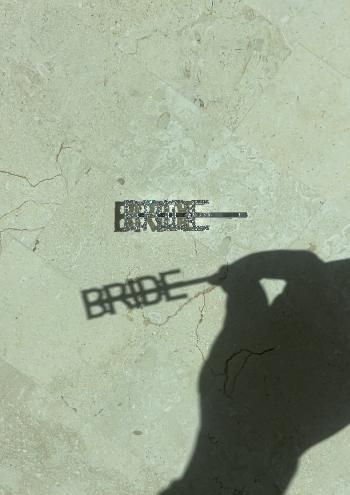 Close-up of our silver 'Bride' Diamante Hair Clip on a marble stone surface. Showing the silver clip and the diamante, sparkling in the light, as well as, showing a clear shadow of the lettering 'BRIDE'. Perfect for all brides