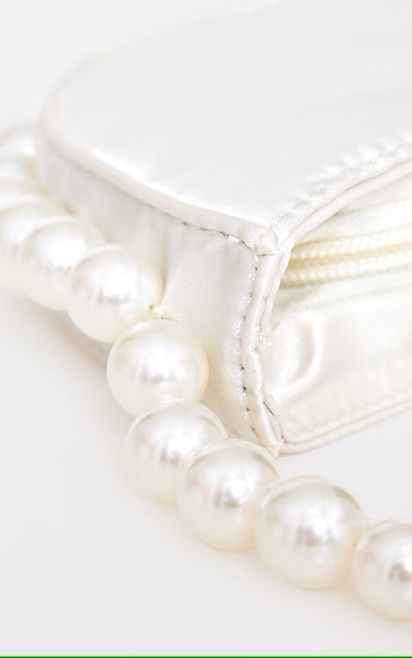 A close up shot of our white silk satin Azalea bag. With a pearl beaded handle that continues around the bottom of the bag. Perfect for adding a touch of class for any formal event or bride to be