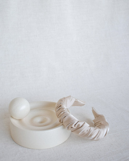 Our Cloud headband against a cream ornament and neutral background. Ruched and wrapped satin/silk around the entire padded band. Adding elegance and class to any bride 