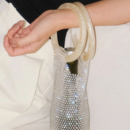 Close up of the ivory resin circular handles of our diamante wine bag. Held over the wrist of a woman, highlighting the sparkle of the diamante mesh bag, containing a bottle. Adding glamour and function to your next dinner party