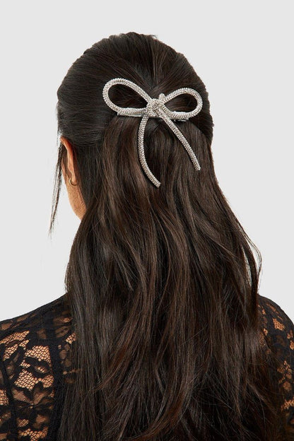 A Woman wearing our Georgie Bow hair clip in a half up half down style. Diamante/rhinestone detail throughout the bow adds all the sparkle to your next outfit.