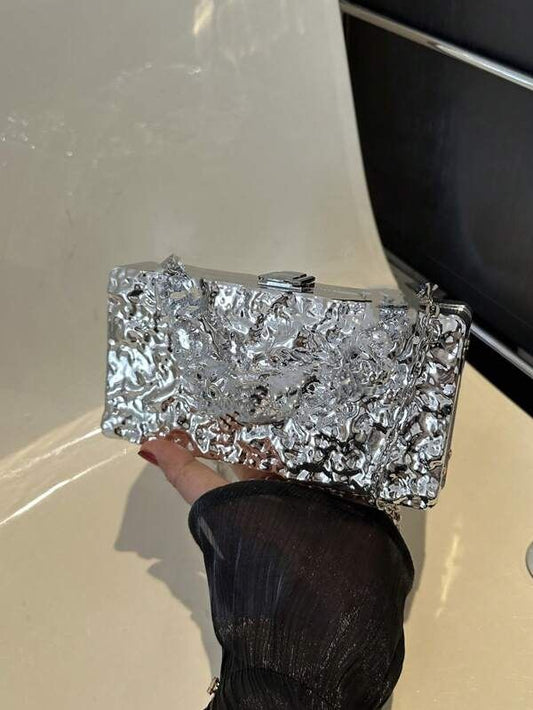 Our Lexi Chrome clutch Bag being held up by a woman, highlighting the shine of the textured chrome design and the compact size. Perfect to add shine to your next evening event