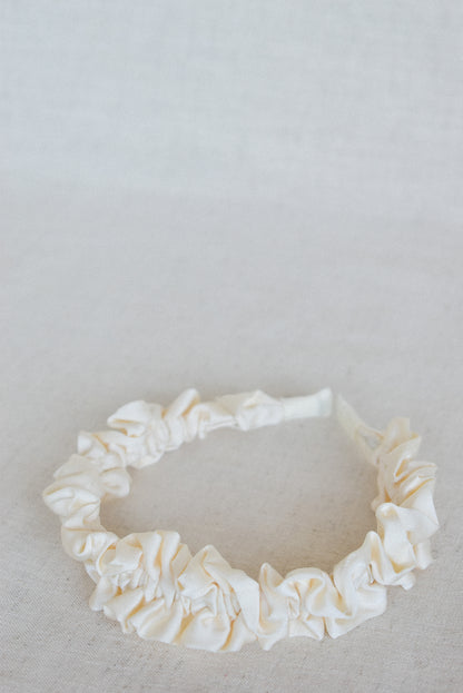 Our Lily headband laying flat, showing a close up of the soft cream ruffled design of the satin/silk material. From ear to ear this design will be a cute addition to any outfit. Perfect for any bridal party or bride on the wedding day. 