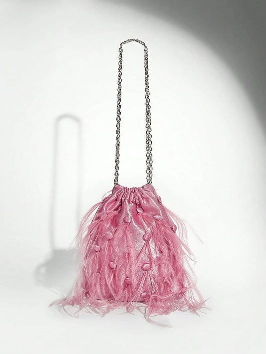 Our Lulu bag against a white background, showing its light pink velvet, drawstring design with soft staggered feathers on one side, with a medium sized silver chain handle. Perfect for adding a pop of colour to your next outfit 