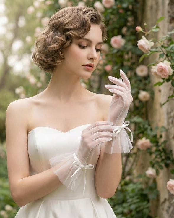 Woman in a white dress with Elegant sheer white tulle wrist-length bridal gloves featuring a delicate mesh bow and ruffled cuff for a modern Bridgerton-inspired wedding look.