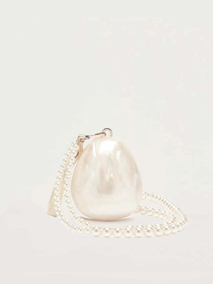 Our Peggy Bag pearl white acrylic egg-shaped mini bag, shown against a white background. Versatile interchangeable handles, as a clutch with a small cream leather wrist strap or a cross body pearl beaded shoulder bag. The ultimate bridal accessory or statement event bag. 