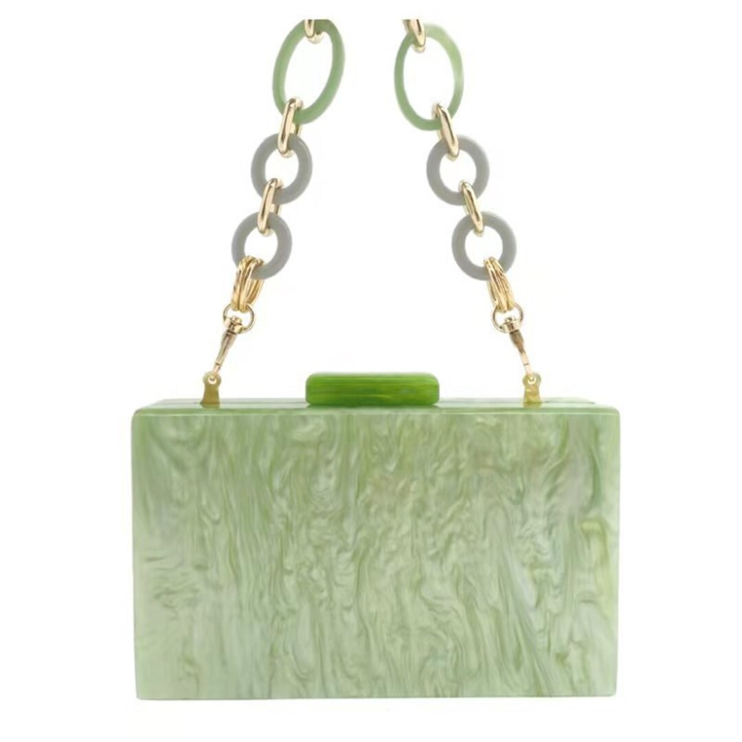 Our rectangular Mint acrylic resin clutch bag shown against a white background with a looped gold and acrylic circle detail handle. The circular loops are a mix of green and grey. Perfect pop of colour to your outfit for your next evening event