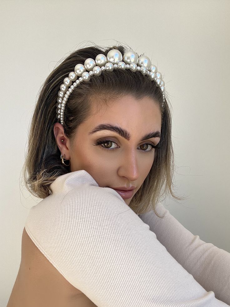 A brunette woman wearing our Orchid headband stacked against another of our smaller pearl headbands. Highlighting a comparison in the size of the pearls and how they increase across the band, they are smallest at the ends and biggest at the middle. Elevating your bridal look on your wedding day or versatile for evening formal events