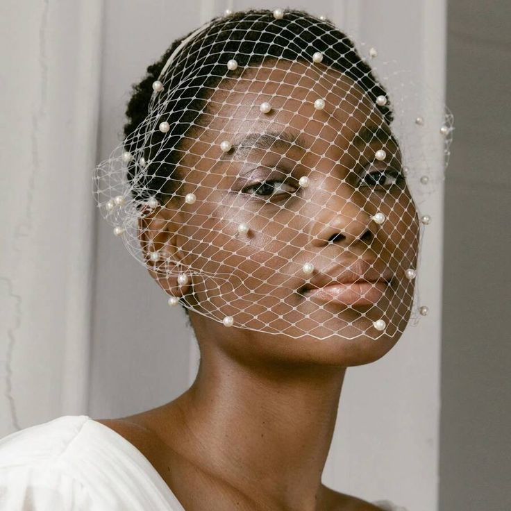 A woman wearing our Paris Veil Headband, showing the white birdcage veil covering the face with delicate netting and pearl detailing. Highlighting the hidden thin band itself. Perfect for brides on their wedding day for timeless looks.