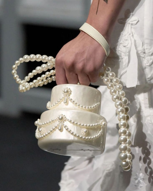 Hand holding a white handbag with pearl details against a blurred background