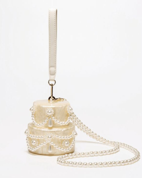 Two-tiered cake-shaped handbag with pearl details on a white background